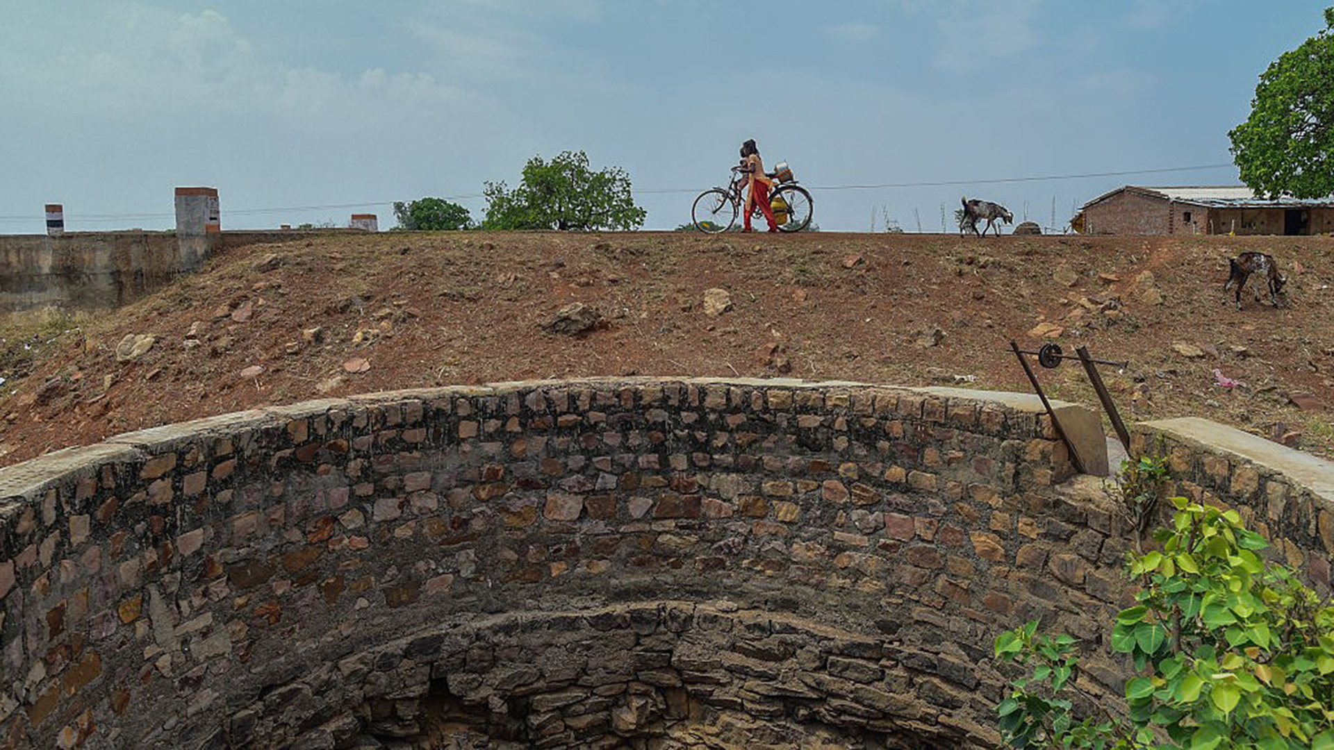 A girl cycles next to a circular well in India.