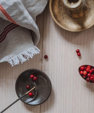 Top down view on lingonberries in a bowl and on a spoon, linen tablecloth, incense and candlestick on wooden table in bright sunlight