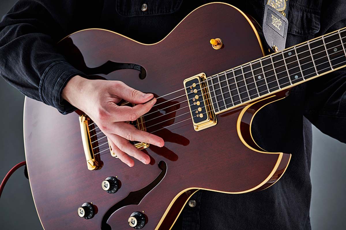 Joe holds his pick between his thumb and the flat pad of his index finger, with his thumb straight or bent slightly back, approaching the string almost parallel.