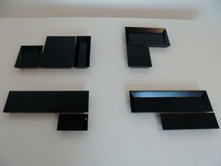 Black tray-like plates in different sizes and shapes (rectangular and square) photographed on a white surface against a white wall