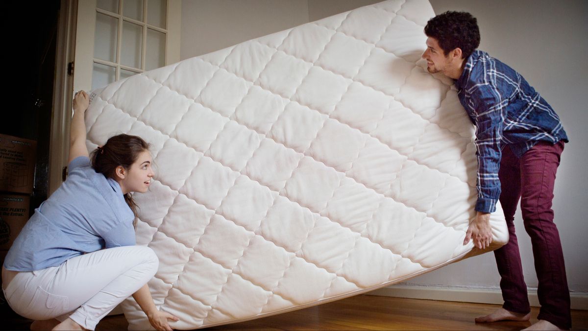 A man and a woman holding each end of a mattress trying to move it