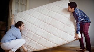 A man and a woman holding each end of a mattress trying to move it