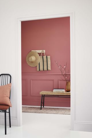 Pink hallway with straw hat against white room with bench