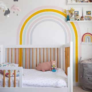 Rainbow mural in a nursery above a cot