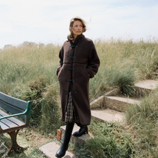 Model walking down steps wearing a brown long sherpa coat, black boots and a plaid dress sold at Nobody's Child