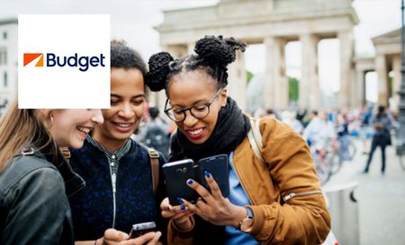 Three women using their mobiles in a tourist area booking a budget rent a car