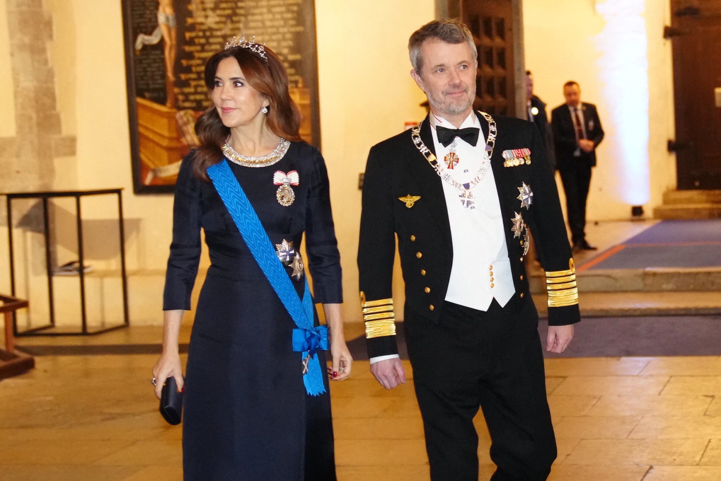 Queen Mary in a navy gown and tiara walking next to King Frederik in a tux