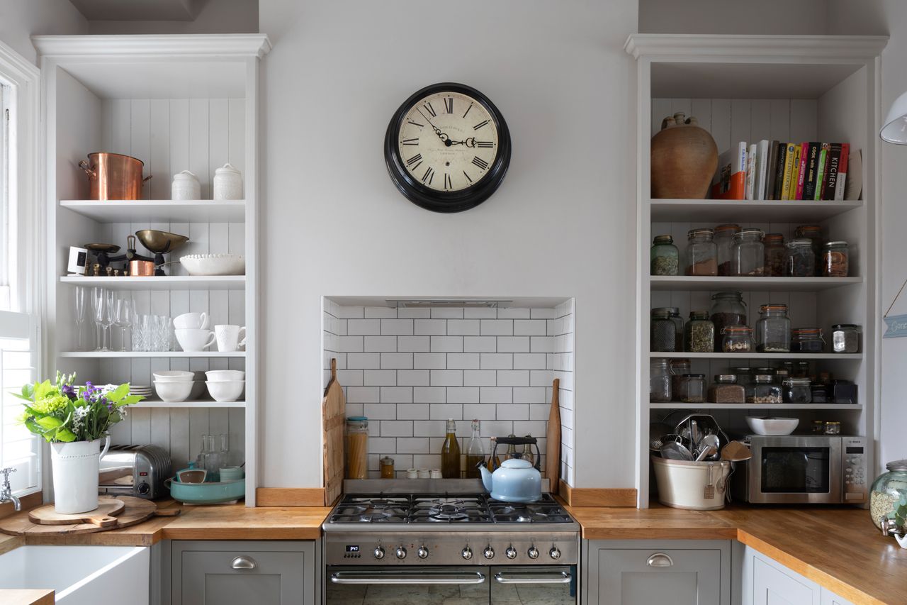 Pippa Jones house: kitchen with grey painted Shaker units, wood worktop, metro tiles in cooker alcove, and open shelving either side of the cooker filled with jars, crockery and cookbooks