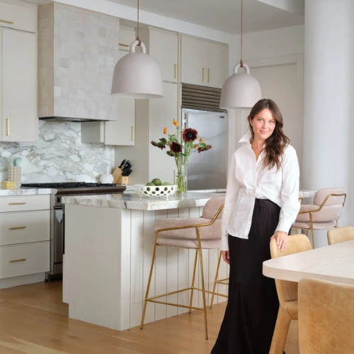 Image of a woman in black pants and a white top standing in a white kitchen.