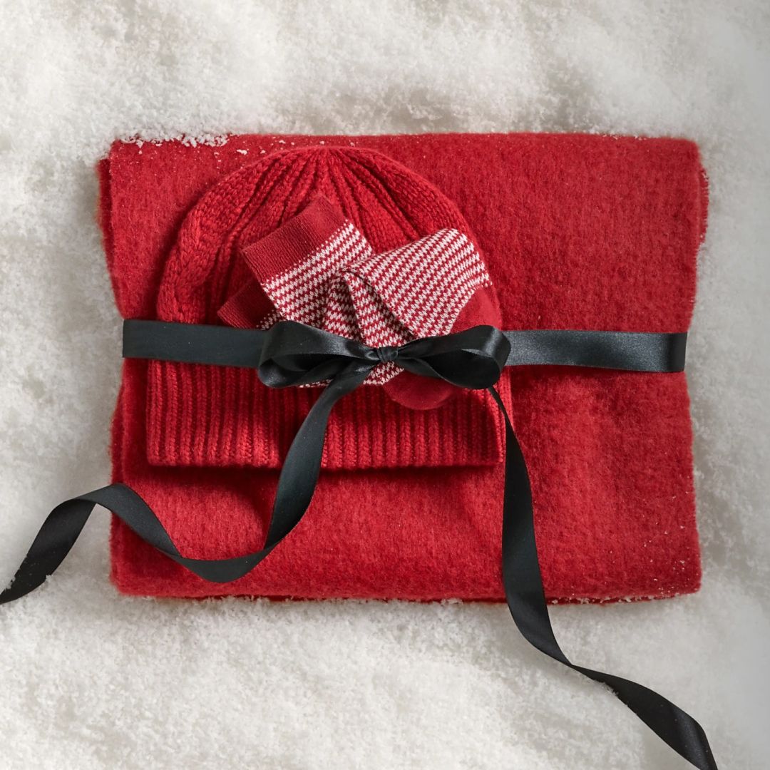 Madewell red scarf, socks, and beanie wrapped in ribbon lying on snow 
