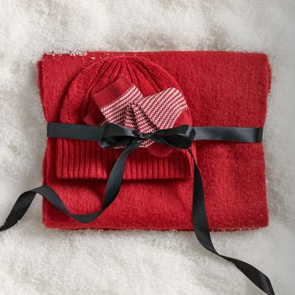 Madewell red scarf, socks, and beanie wrapped in ribbon lying on snow 