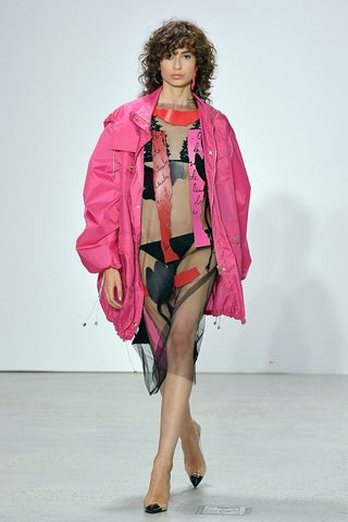 Model wearing a pink coat walking down a catwalk