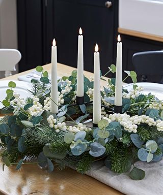 eucalyptus and white christmas berry wreath with white taper candles on a kitchen table