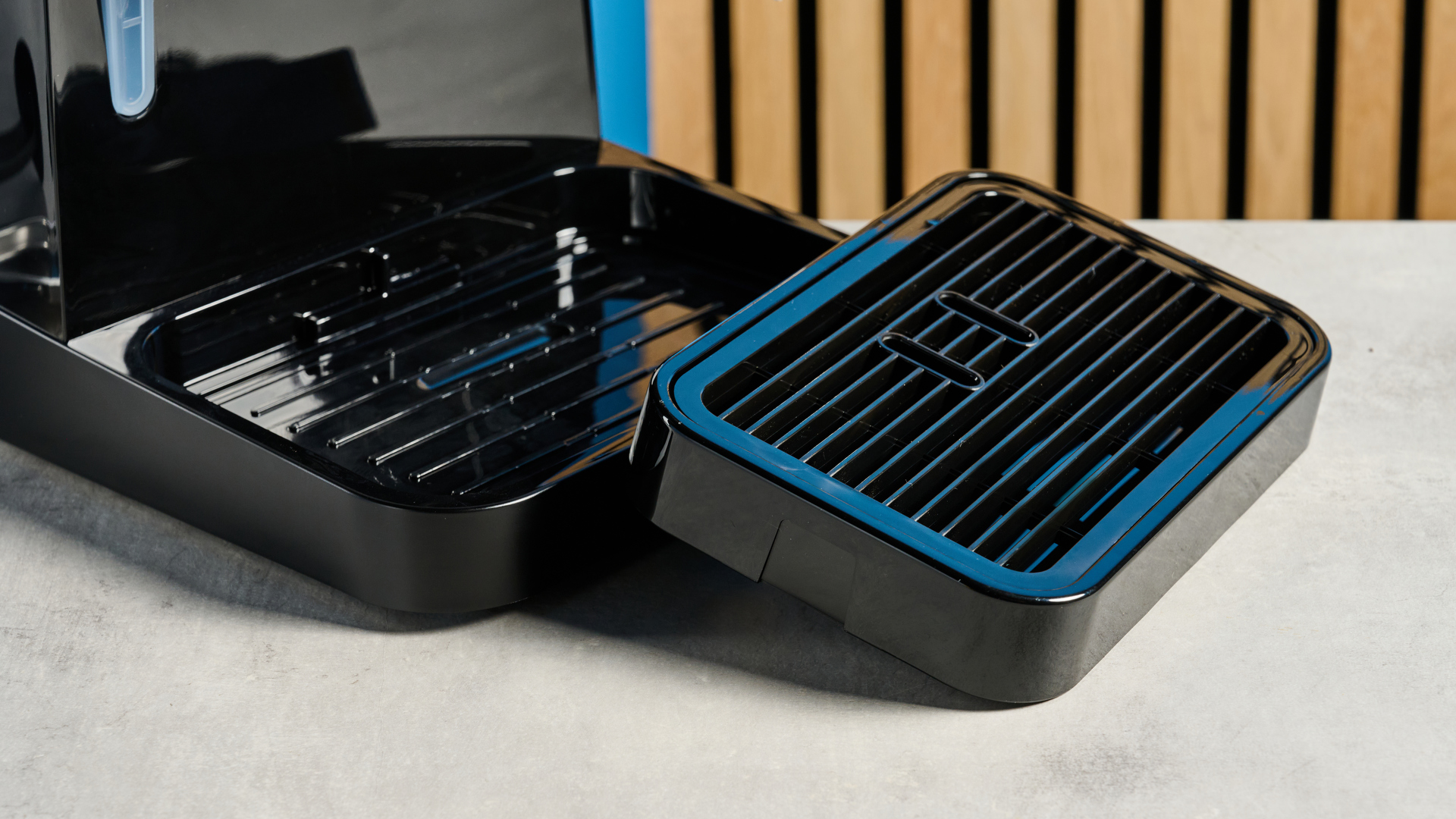 the de'longhi stilosa espresso machine in black, with one portafilter, a dial for espresso and milk steaming, and a plastic tamper, photographed against a blue background