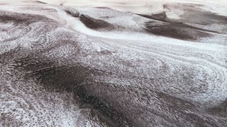 wispy snow stretches across a reddish-brown landscape