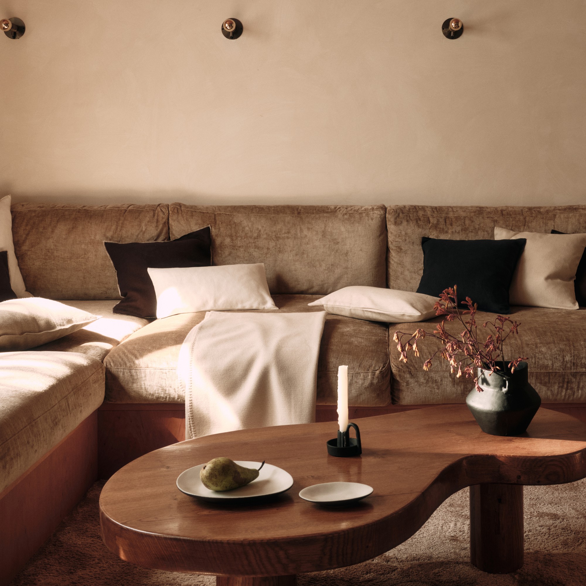 A living room with a curved coffee table and autumn foliage in a vase