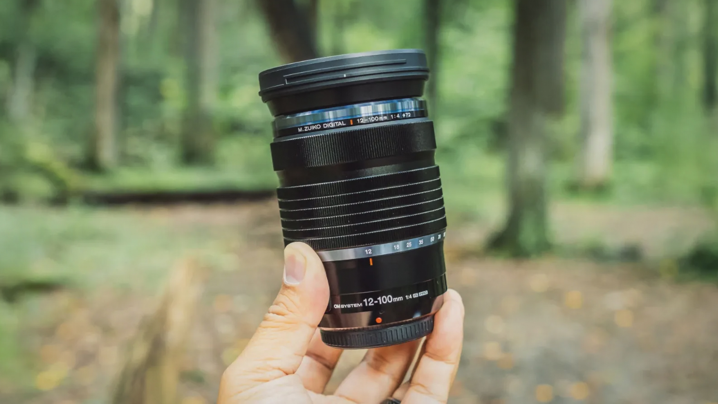 Olympus M.Zuiko 12-100mm f/4 IS Pro being held by hand, outdoors