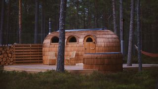 wooden shingle covered sauna in garden with hammock and trees in background