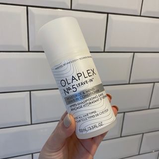 Image showing hand holding the Olaplex No.5 Leave-In Conditioner against a white tiled background