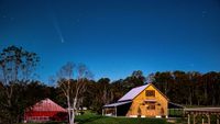 a fuzzy white streak in the night sky above a red barn