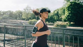 sportswoman listening music through in-ear headphones while jogging on bridge in city