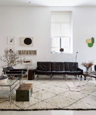 A white and beige living room with minimalist decor, black leather sofa, wall-mounted artwork and Berber rug.