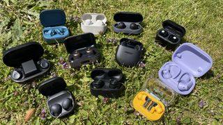 A selection of earbuds, all on a grassy lawn on a sunny day