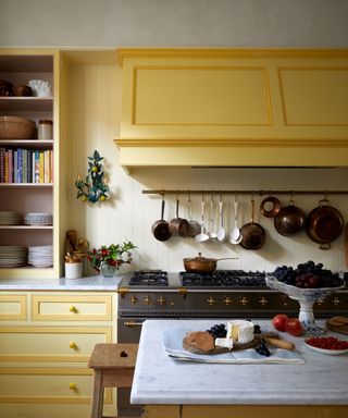 Kitchen with yellow units, cream walls, parquet flooring and large range cooker with saucepans hanging on the wall above.