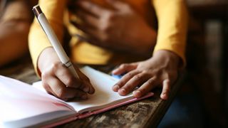 A girl writes in a notebook with her right hand.