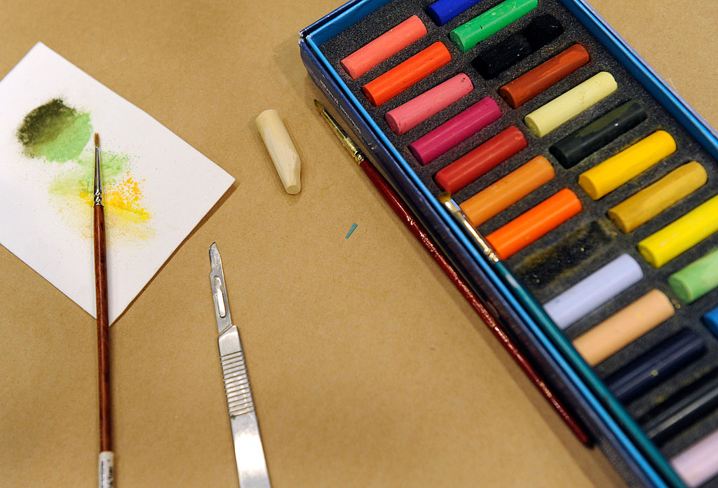 pastels in a box with a scalpel and paintbrush next to them