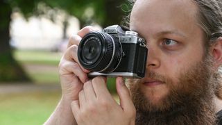 Man holding a Nikon Z fc up to his eye with trees in the background