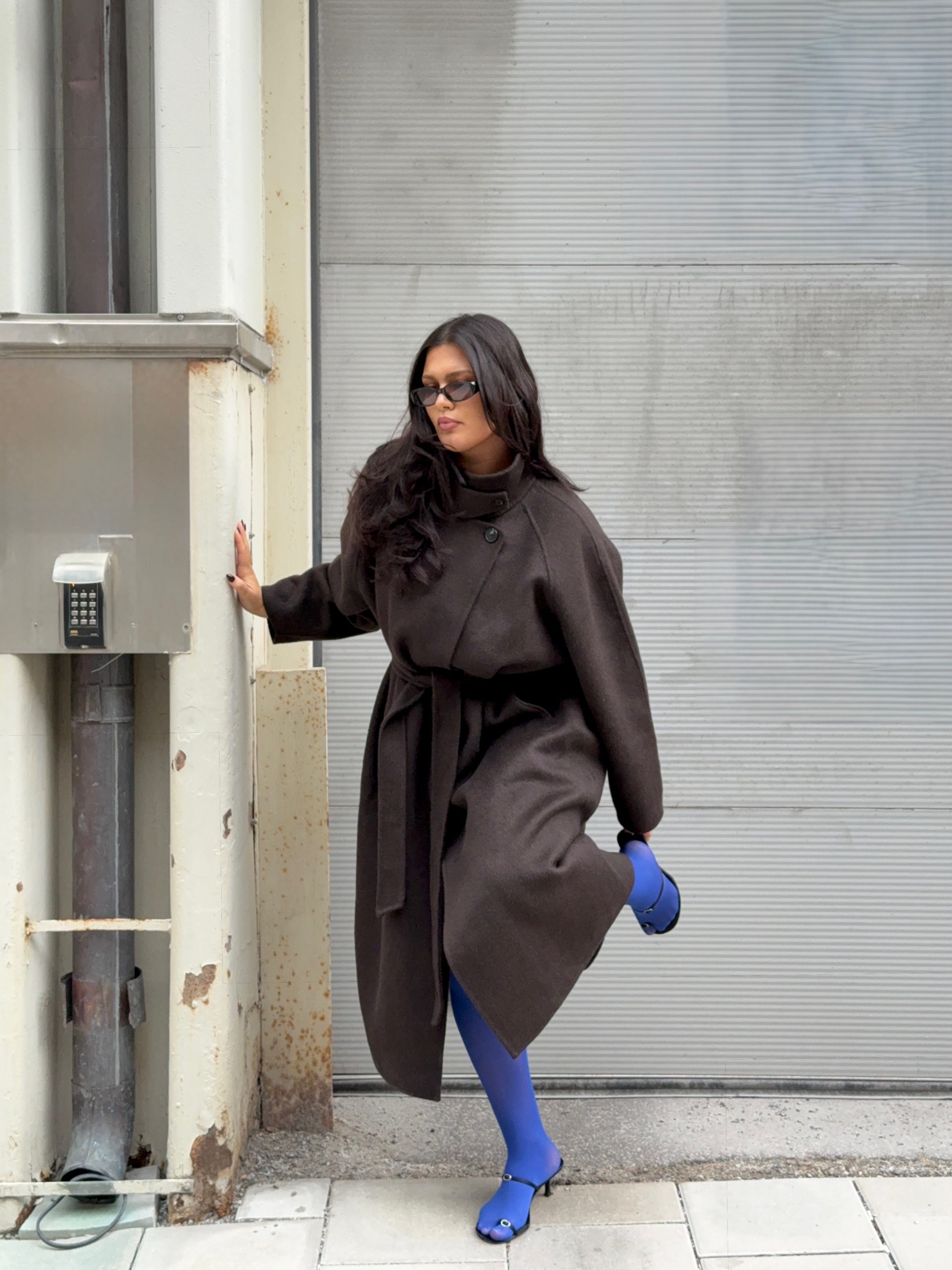 @isabellecoheen wears cobalt blue tights with black strap sandals and a brown coat