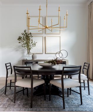 dining room with black round dining table and chairs in room with neutral walls textured wall art and contemporary chandelier