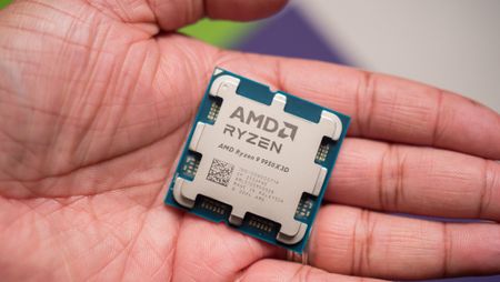Hand holding an AMD Ryzen 9 7950X3D processor. The chip is square with metallic surface and visible engravings, evoking a sense of advanced technology.