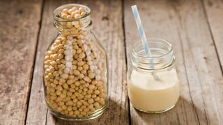 Jar of soy beans next to mason jar half filled with soy milk with blue and white straw