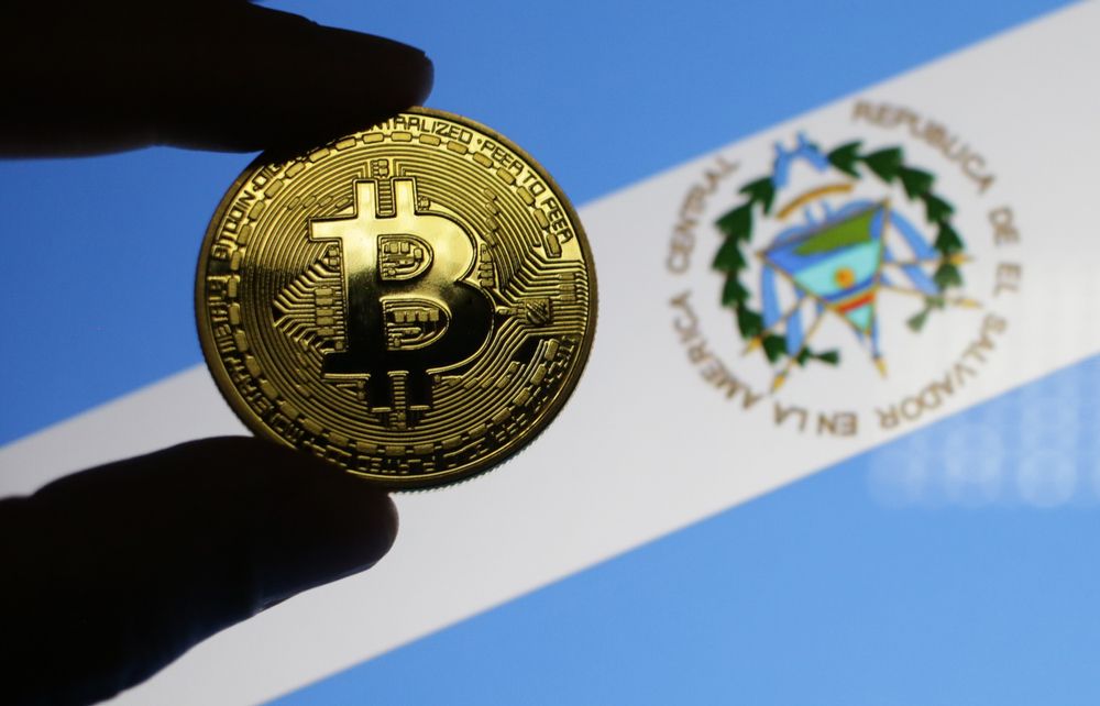 Fingers holding a &amp;#039;bitcoin&amp;#039; in front of the flag for El Salvador