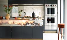 Sleek black kitchen with deep white marble worktop with backlit stone elements