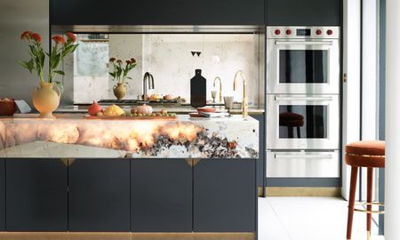 Sleek black kitchen with deep white marble worktop with backlit stone elements