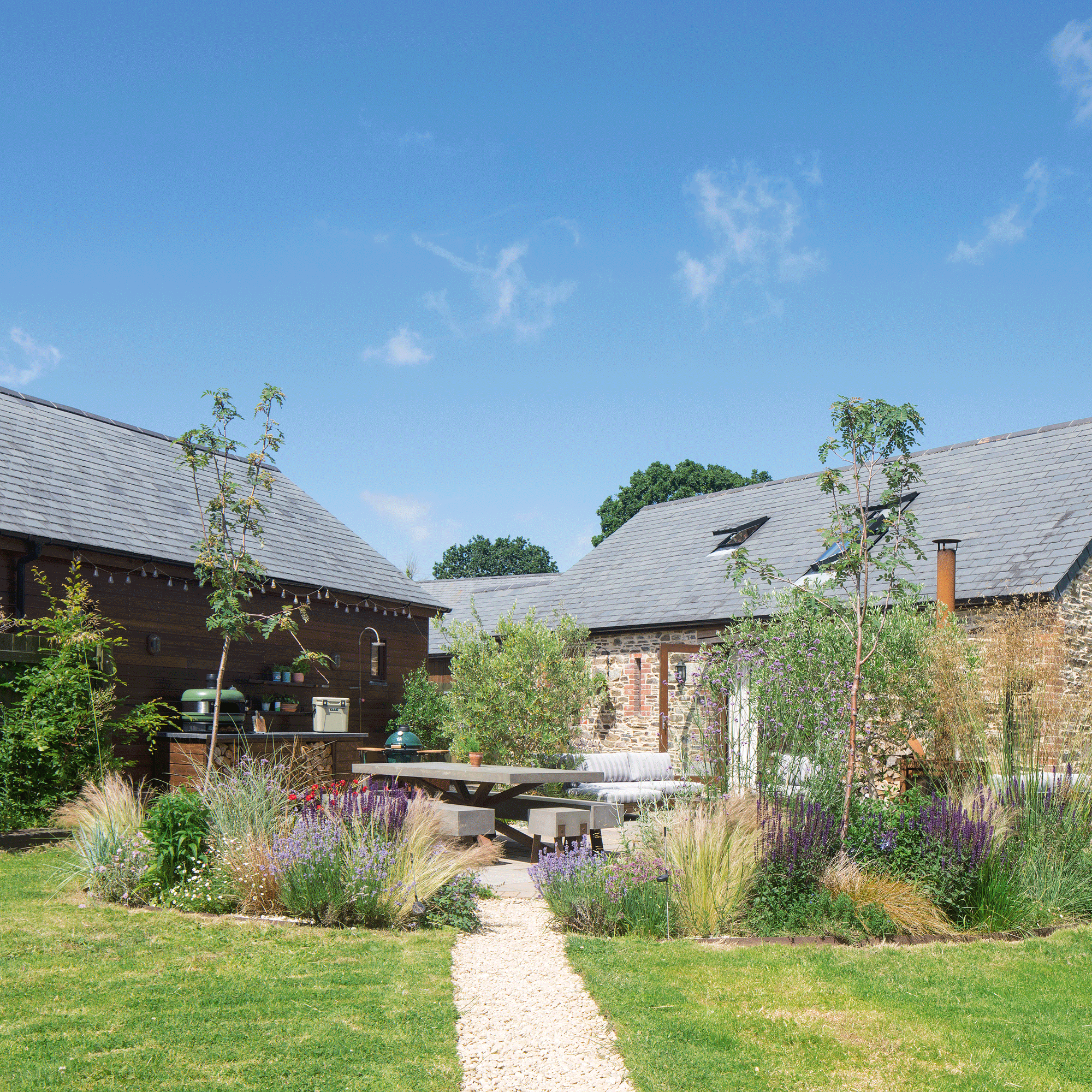 a garden with a lawn with a pebbled pathway through the middle leading to a dining area and outdoor kitchen