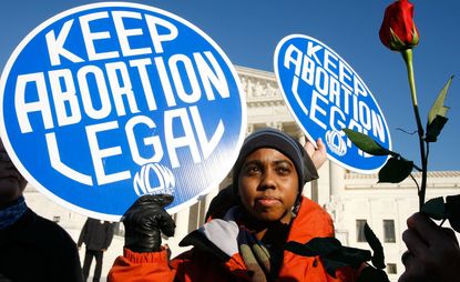 SCOTUS Roe v Wade. Local pro-choice activist Lisa King holds a sign in front of the U.S. Supreme Court as a pro-life activist holds a rose nearby during the annual "March for Life" event January 22, 2009 in Washington, DC. The event was to mark the anniversary of the 1973 Roe v Wade Supreme Court abortion ruling