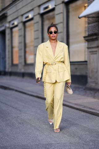 Ellie Delphine mengenakan kacamata hitam, jaket blazer besar berwarna kuning pucat pastel, ikat pinggang, celana melebar, di luar Mark Kenly Domino Tan, selama Copenhagen Fashion Week