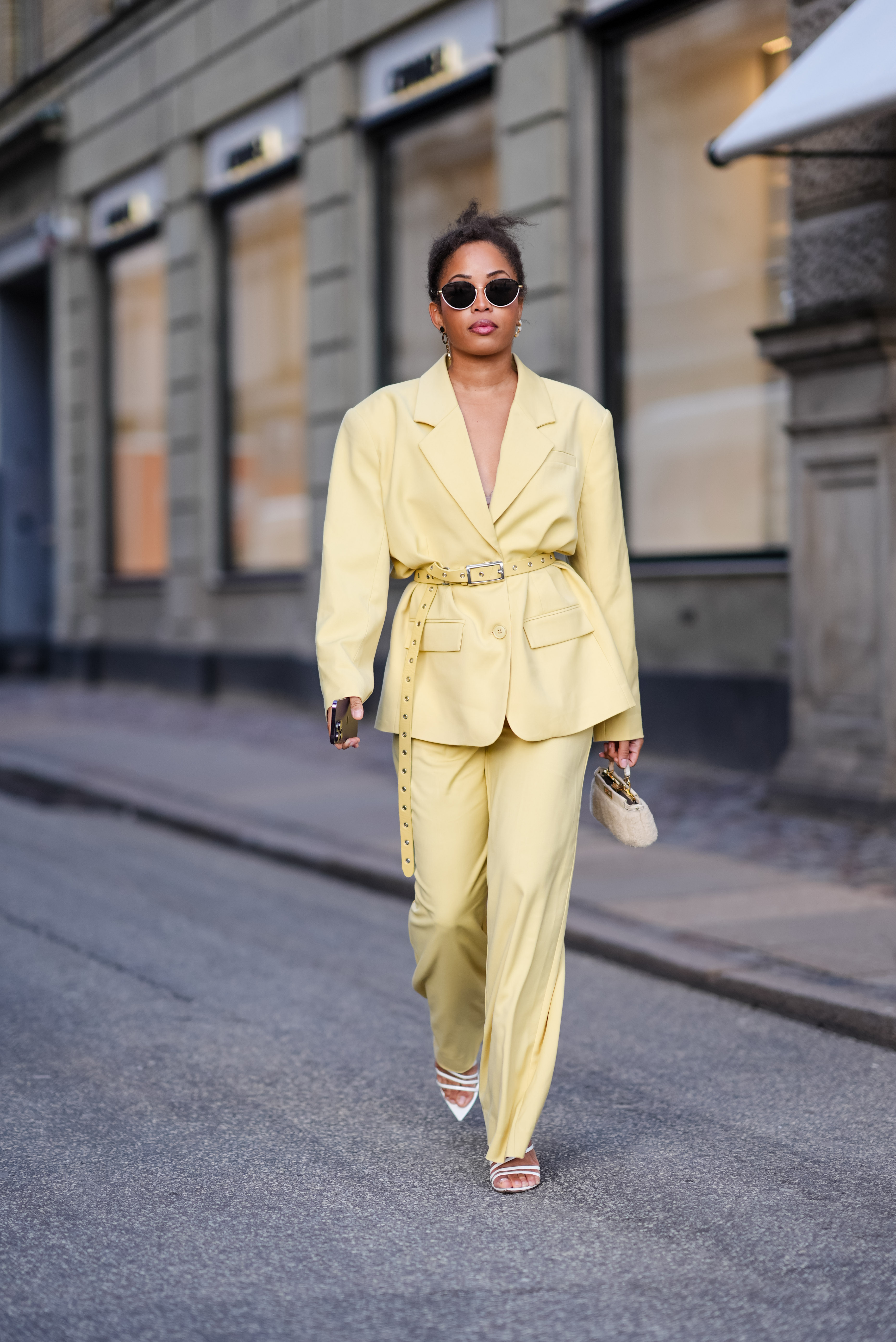 Ellie Delphine wears sunglasses , a pastel pale yellow oversized blazer jacket , a belt, flared pants , outside Mark Kenly Domino Tan, during the Copenhagen Fashion Week