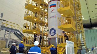 Workers stand at the base of a test stand holding the top segment of a rocket.