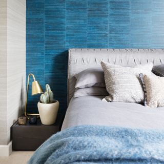 how to make a guest room look more expensive, small bedroom with textured wallpaper, grey bed, grey and pale blue bedding, small chest as side table, brass table lamp, cactus