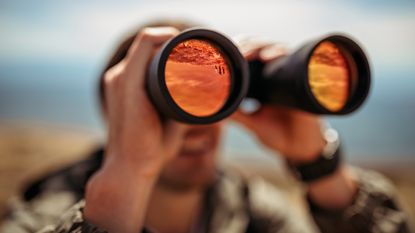A man looks into the distance with binoculars.