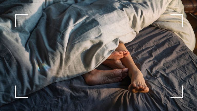 Feet of a couple in bed together under dark blue sheets to illustrate best sex trends 2022