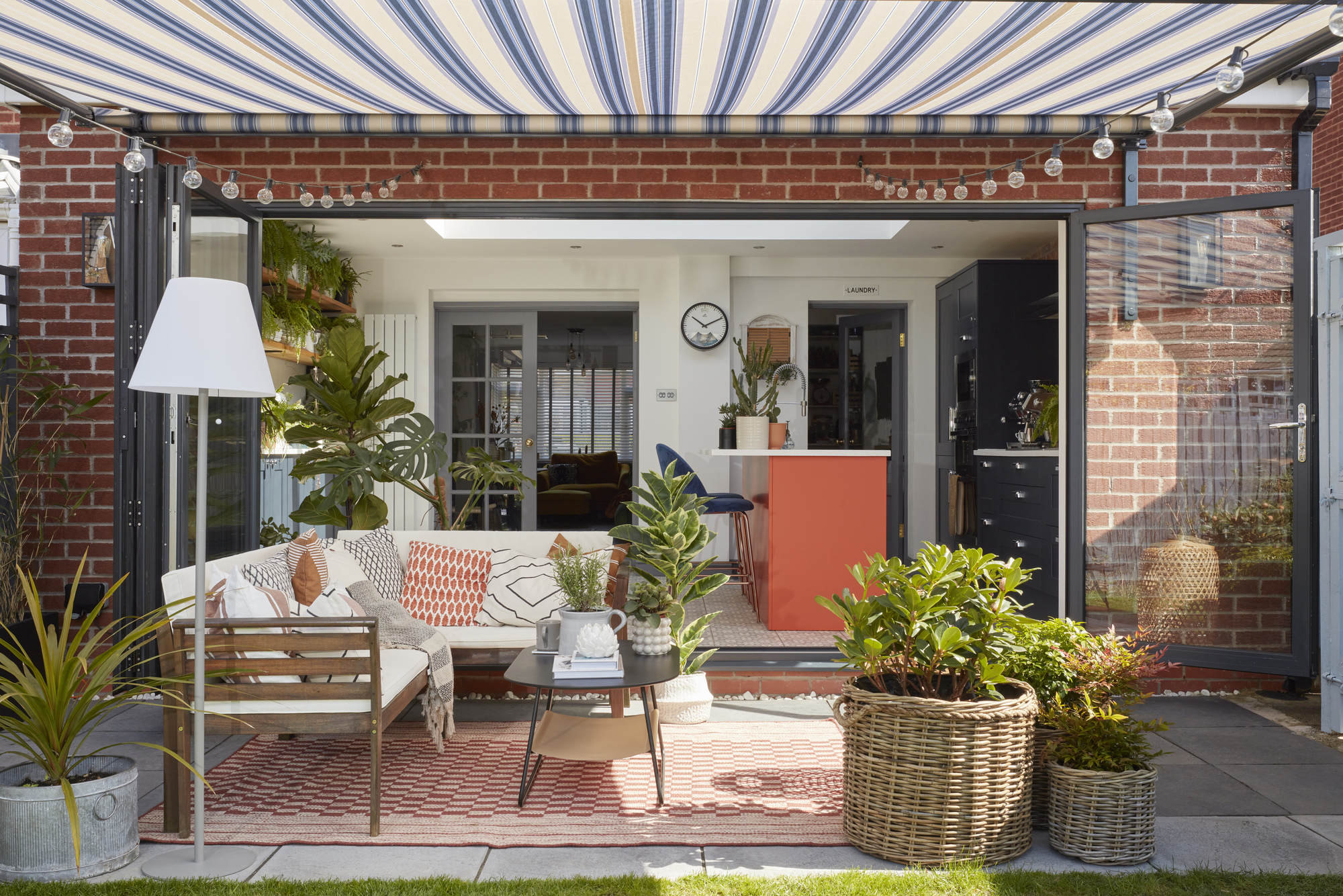 A patio area with an blue and white striped awning attached to the house offering shade for an outdoor seating area