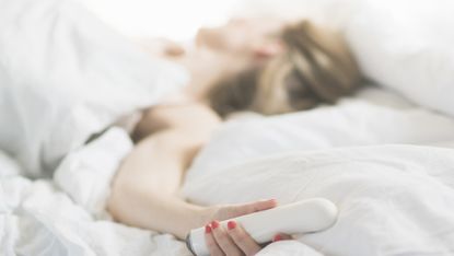 Woman in bed holding sex toy - stock photo