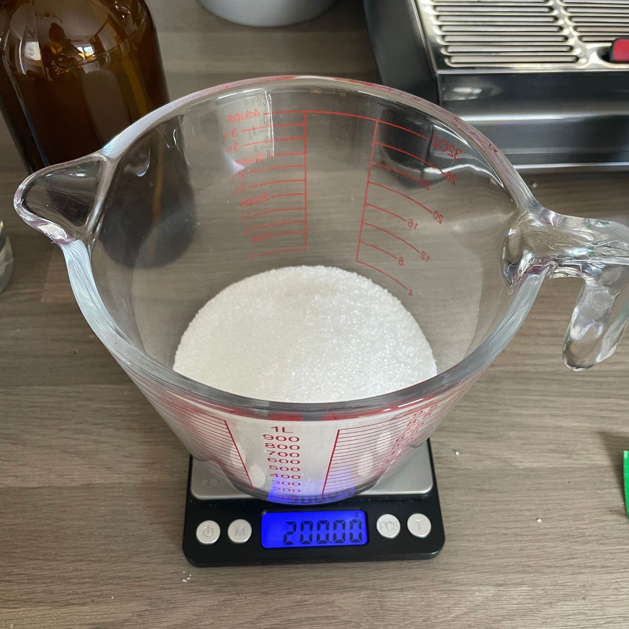 A mound of white citric acid in a glass jug, on metalic measuring scales showing 200g on the digital screen