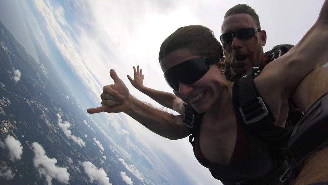 Ashlee Autore, an atmospheric data scientist at the NASA Langley Research Center, went skydiving on an overcast day in Louisiana. Above her are thin, ice-bearing cirrus clouds, and below, a smattering of water-laden cumulus clouds. She is doing a tandem skydive and has a man attached just behind her.